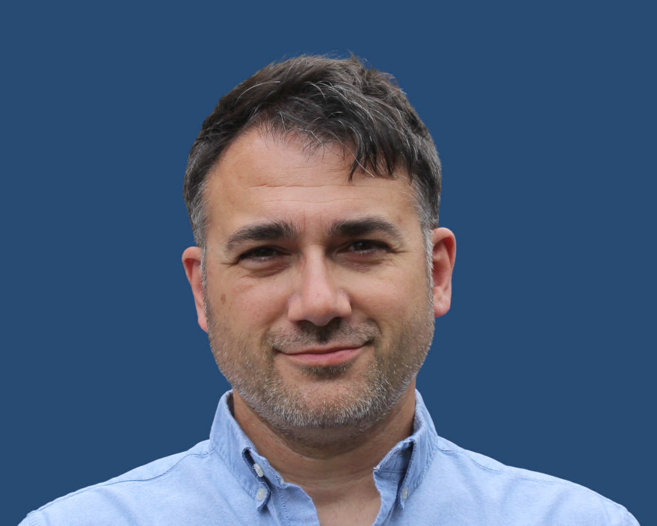 A headshot of Robin Hodges. A white man with short dark hair, brown eyes, and light stubble. He is wearning a shirt and looking directly at the camera.